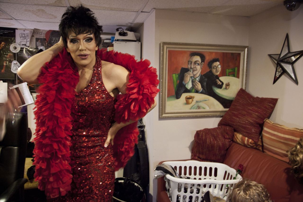 A group portrait of drag performers seated together in a restaurant booth.