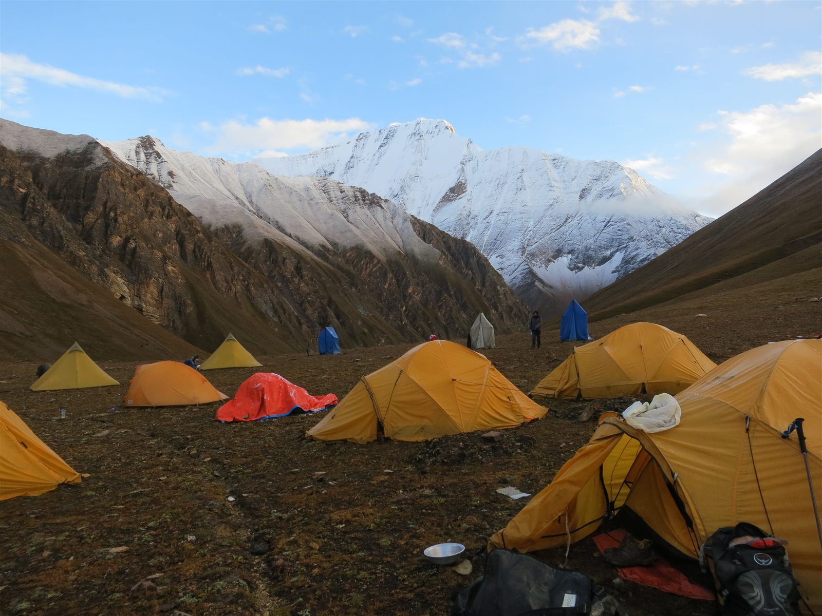A high-altitude camp at dawn: a dozen tents pitched on brown scree below a snow-covered ridge.